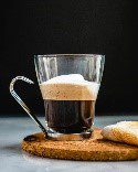 A glass of coffee on top of a wooden board.